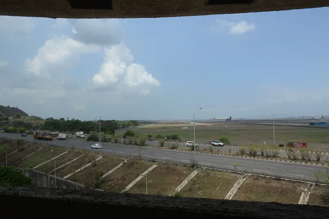Seen through a concrete opening: the highway, the airfield beyond it and a wooded hill to the left — Dhruva, Karanjade