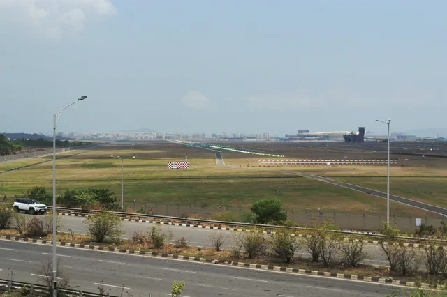 Green runway lights and a red-and-white marker board on the airfield, over the perimeter road — Dhruva, Karanjade