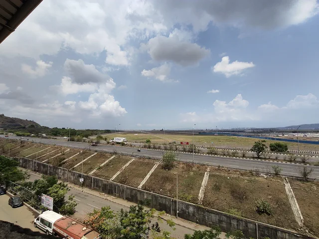 The compound wall and its drainage channels below, the airfield and a wide cloudy sky beyond — Dhruva, Karanjade
