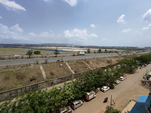 Cars parked on the unmade road below, the highway curving away past the airfield — Dhruva, Karanjade
