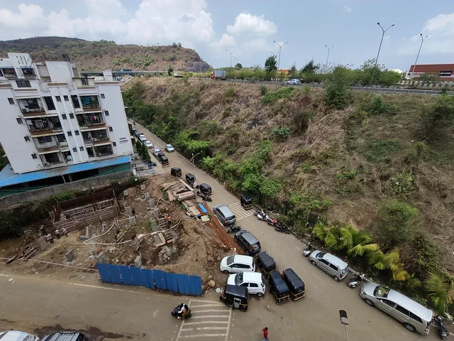 Autorickshaws and cars parked along the road below, against the cut hillside and a neighbouring block — Dhruva, Karanjade