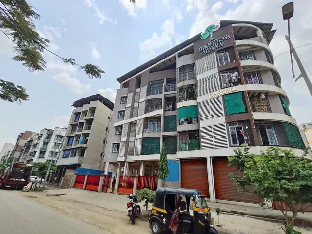 Street-level view of the name board and red shop shutters, an autorickshaw parked outside — Dhruva, Karanjade