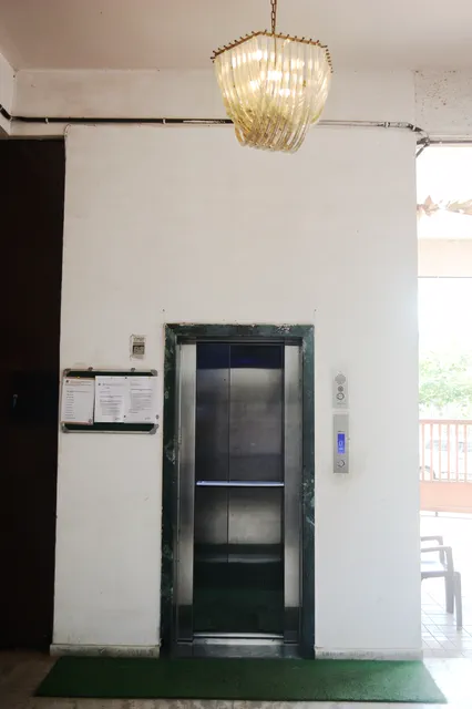 Stainless-steel lift doors on the ground-floor landing, notices posted on the wall alongside — Dhruva