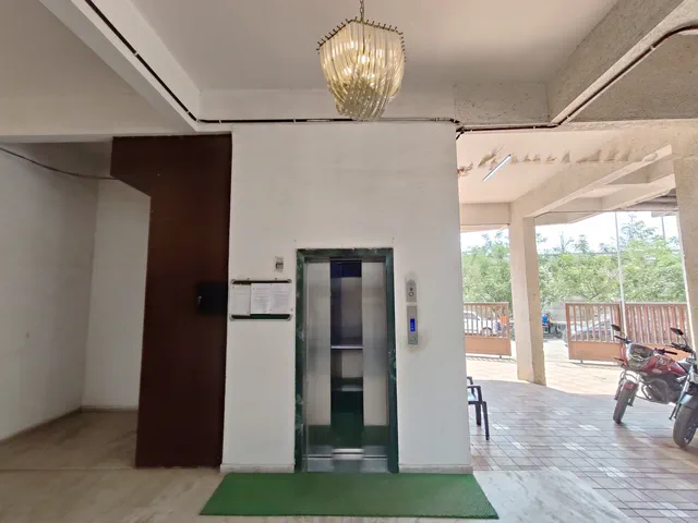The lift landing opening out to the covered stilt parking, a motorcycle parked beyond — Dhruva