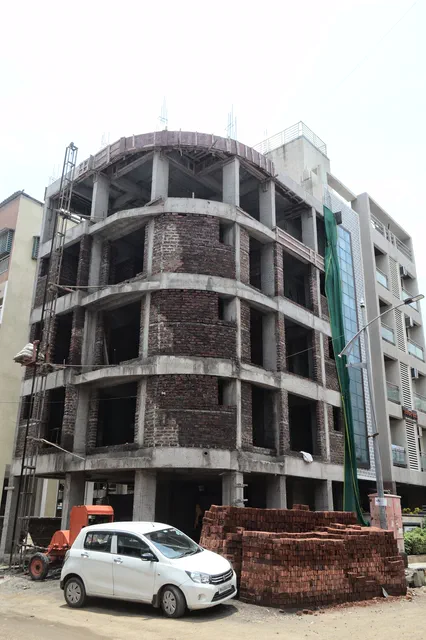 The frame going up in brick and concrete, a mixer and a parked autorickshaw at the roadside — Ishaan, Karanjade
