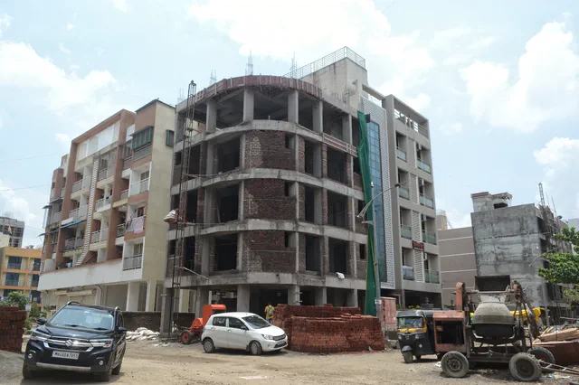 The curved corner in red brick infill, a stack of bricks and a car on the unmade road — Ishaan, Karanjade