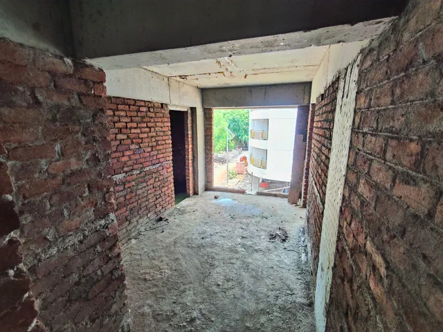 Bare brick walls and a raw floor in a 1RK, the opening framing the building next door — Ishaan