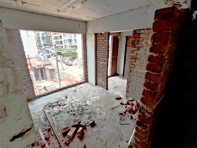 A wide corner window opening over the street in a 1RK, brick and rubble still on the floor — Ishaan