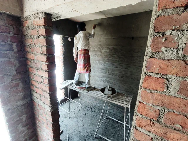 A worker rendering the wall of a narrow brick-lined space, standing on a folding platform — Ishaan
