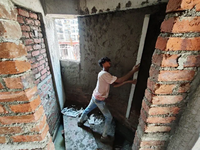 A worker running plaster down a doorway reveal, the brickwork still open beside it — Ishaan