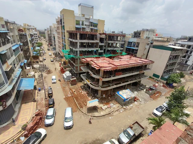 The building rising mid-street, cars and trucks nose to tail along the road below — Prithvi, Karanjade