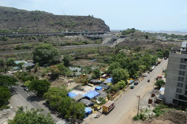 Blue-tarped stalls and parked vehicles on the road below, the cliff-topped hill across the skyline — Rudra, Karanjade