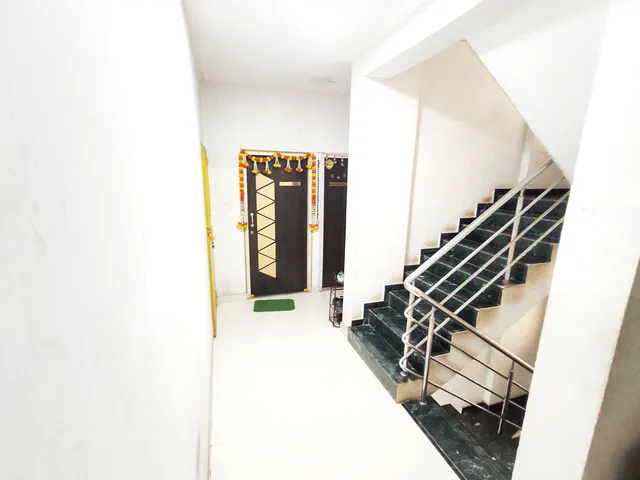 A garlanded flat door off the tiled landing, the staircase and its steel railing alongside — Rudra
