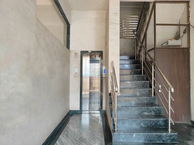 Lift doors and the dark marble staircase side by side at the entrance, railing rising past — Rudra, Karanjade