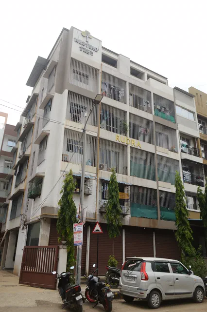 Climbing plants up the front of the finished building, green balcony panels and shuttered shops below — Rudra, Karanjade