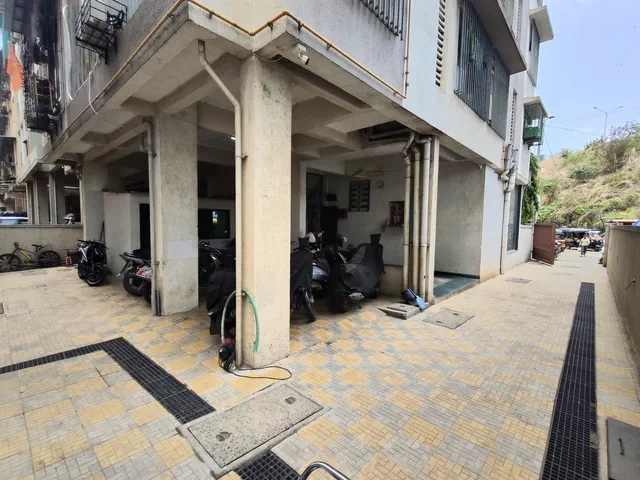 Motorcycles lined up between the columns of the stilt parking, seen in from the driveway — Rudra