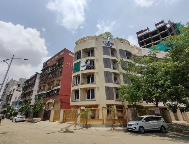 Seen along the street past the lamp post, the neighbours crowding in on either side — Shaurya, Karanjade