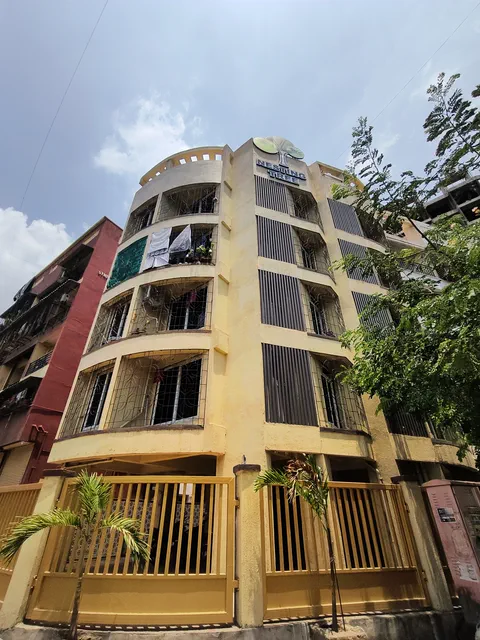 The corner of the building from the roadside, balconies stacked above the yellow railing — Shaurya, Karanjade