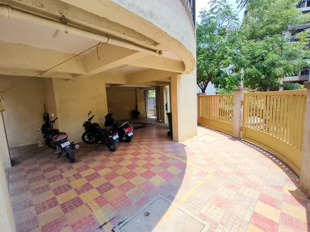 Motorcycles under the building beside the yellow timber fence, the trees just beyond it — Shaurya