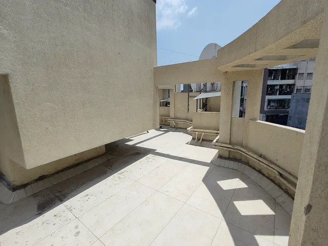 Tiled rooftop deck between curved parapet walls, a dish antenna and the neighbours beyond — Shaurya, Karanjade