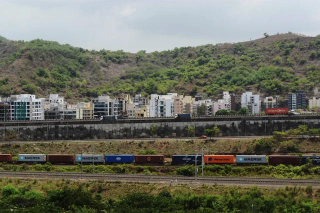Container wagons standing on the railway line, apartment blocks and the green hillside behind — Shikhar, Karanjade