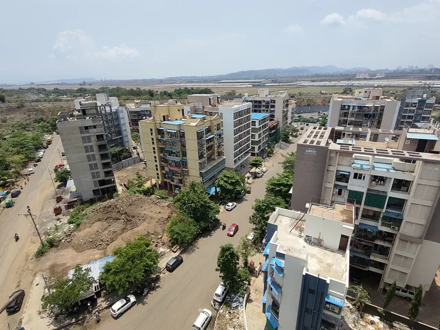 Low-rise apartment blocks along the streets below, the airport flatland and hills on the horizon — Shikhar, Karanjade