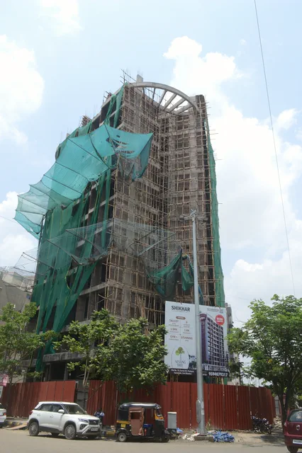 The tower under scaffolding and green safety netting, its curved crown against the sky — Shikhar, Karanjade