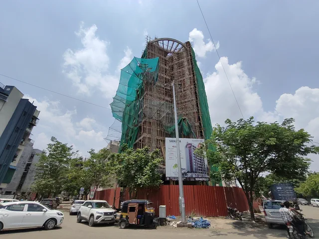 The netted tower from across the road, red site hoarding at its base and an autorickshaw waiting — Shikhar, Karanjade